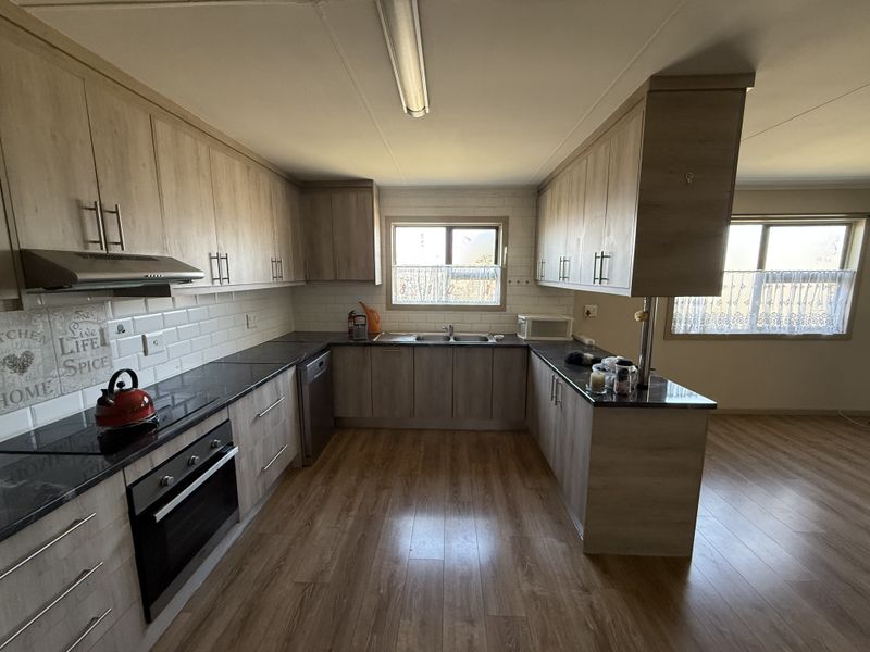 A functional kitchen featuring light wood-grain cabinetry, dark laminate countertops, a subway tile backsplash, and integrated appliances including an oven and extractor fan.