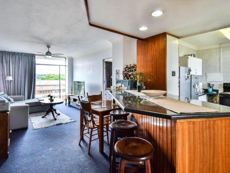 Open-plan living and kitchen area featuring a granite breakfast bar, recessed lighting, and direct access to a balcony through sliding glass doors.