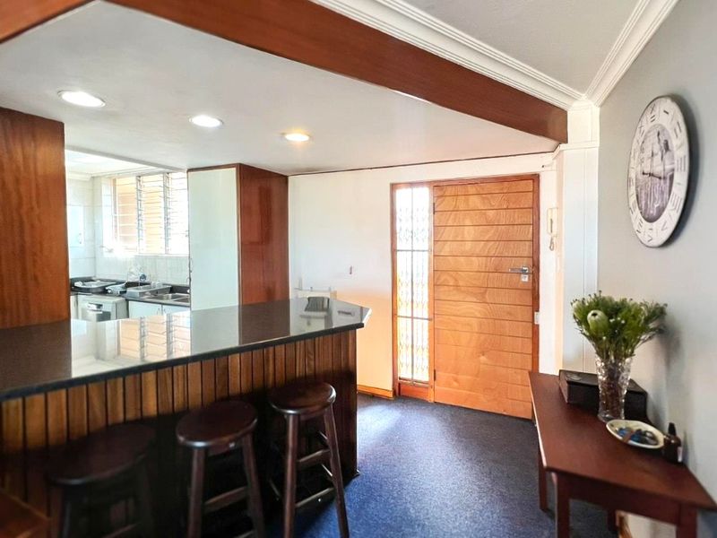 Open plan living area featuring a breakfast bar, wooden front door, and recessed lighting, seamlessly connecting to the kitchen space.