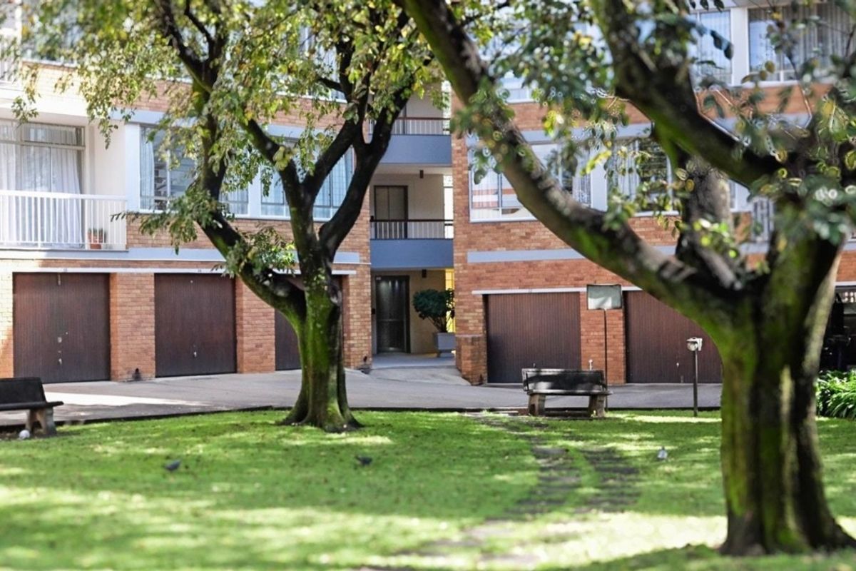 View of the apartment complex rear courtyard featuring brick facade, multiple garage doors, balconies, and a shared garden area.