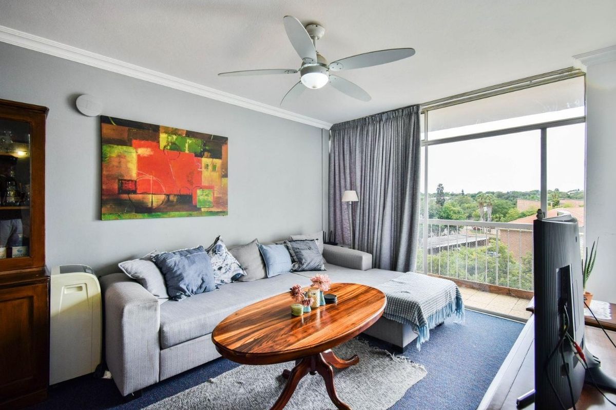 A comfortable living room featuring a ceiling fan, crown molding, and a large sliding glass door providing access to a balcony with exterior views.