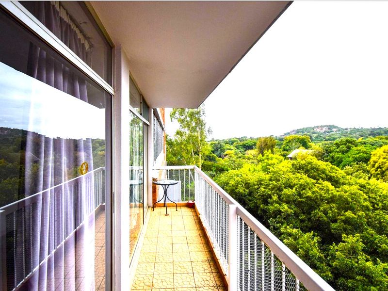 A covered balcony featuring tiled flooring and a metal balustrade, offering elevated views of the surrounding greenery.