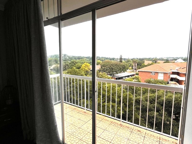 A balcony with tiled flooring and a metal balustrade, accessible via a sliding glass door, offering an elevated view of the surrounding neighborhood.