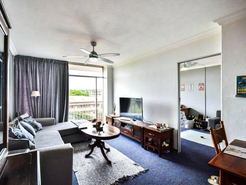 A living room featuring carpeted flooring, a ceiling fan, and a sliding glass door providing access to an outdoor area.