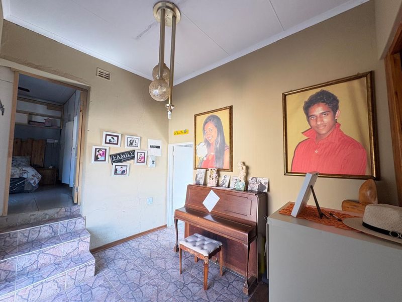 A living area featuring tiled flooring and a stepped transition to an adjacent room, with visible wall surface wear requiring maintenance.