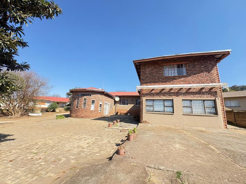 Rear view of a multi-level face brick house featuring a large paved driveway and concrete apron area under a clear blue sky.