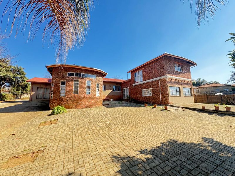 Front exterior view of a multi-level brick house featuring a paved driveway and distinctive curved architectural design.