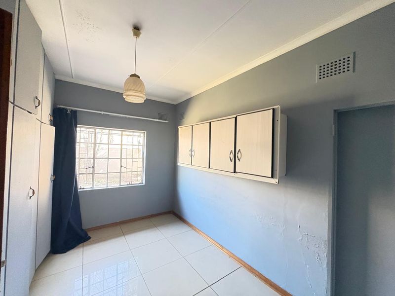 An empty bedroom featuring tiled flooring, built-in cupboards, and security bars on the window, requiring minor cosmetic repairs to the walls.
