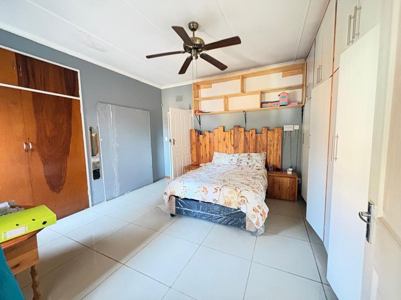 Spacious bedroom featuring tiled flooring, built-in cupboards, and a ceiling fan, offering a functional layout with potential for cosmetic updates.
