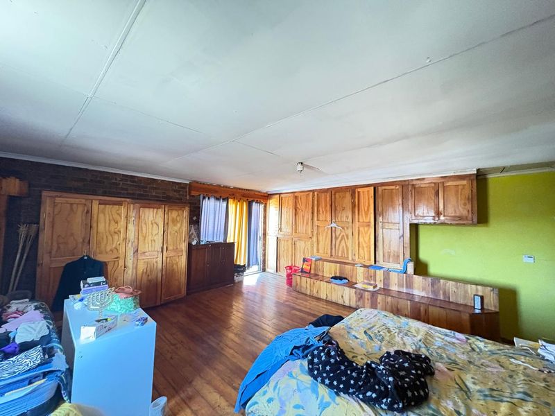 Spacious bedroom featuring extensive built-in wooden cabinetry, exposed brick accents, and wooden flooring, offering significant potential for modernization and aesthetic improvement.