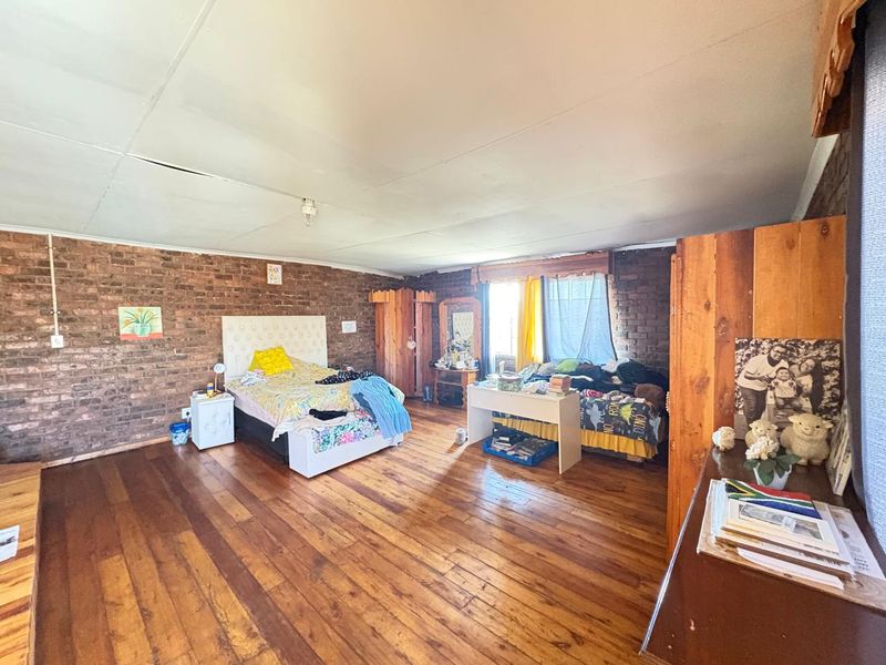 Spacious bedroom featuring exposed brick walls and timber flooring, requiring some ceiling repairs and cosmetic updates to enhance its appeal.