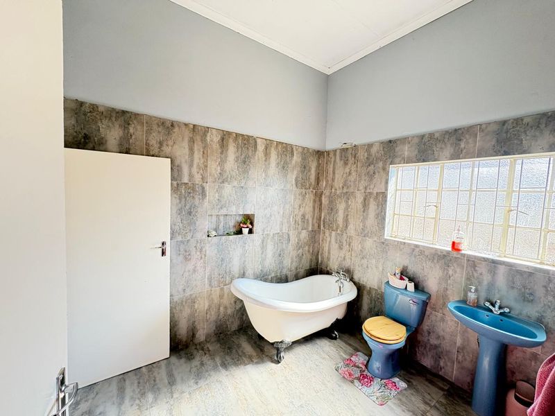 Bathroom featuring a clawfoot bathtub, pedestal basin, and toilet, finished with full-height wall tiling and a tiled floor.