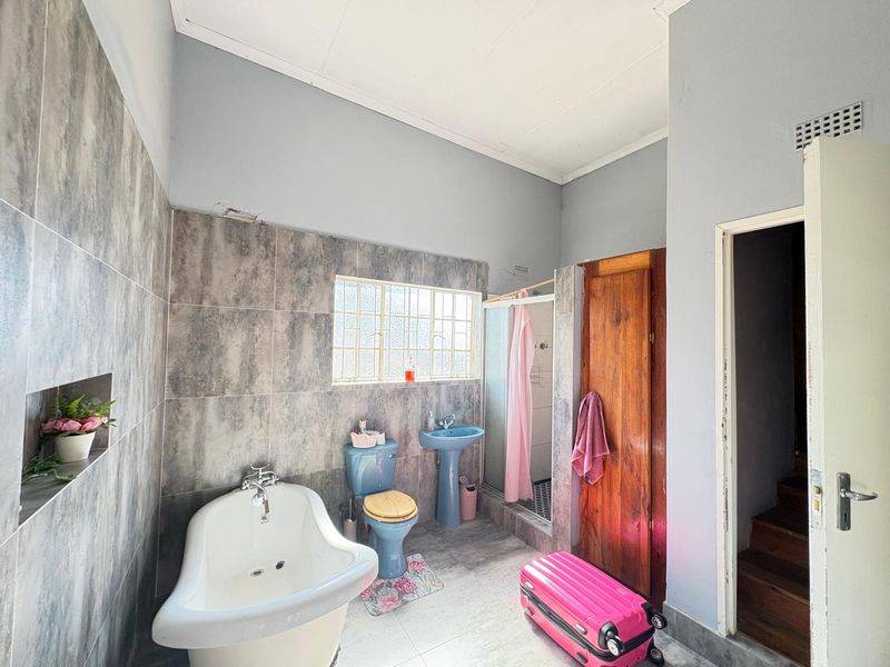 A bathroom featuring a freestanding bathtub, pedestal basin, toilet, and shower enclosure with grey tiled walls and flooring.