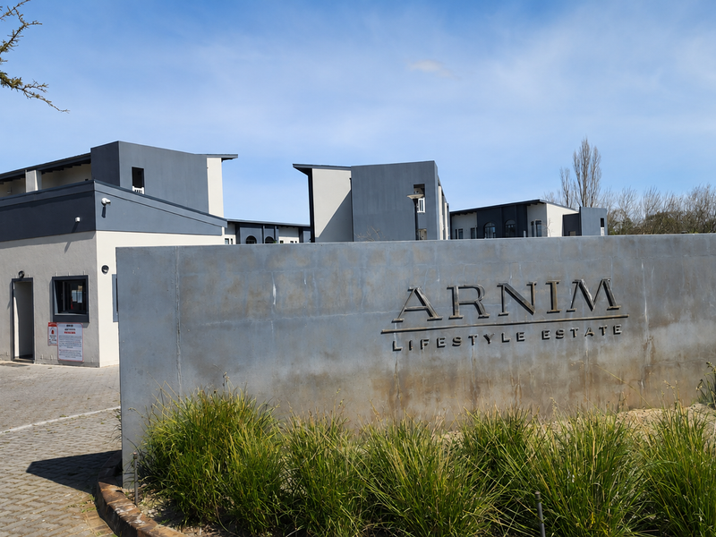 Entrance view of Arnim Lifestyle Estate featuring a modern security gatehouse, paved driveway, and prominent estate signage.