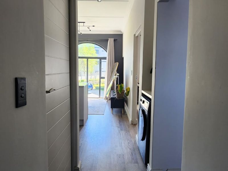 A bright, modern hallway featuring laminate flooring and clean finishes, leading towards an open-plan living area with natural light.