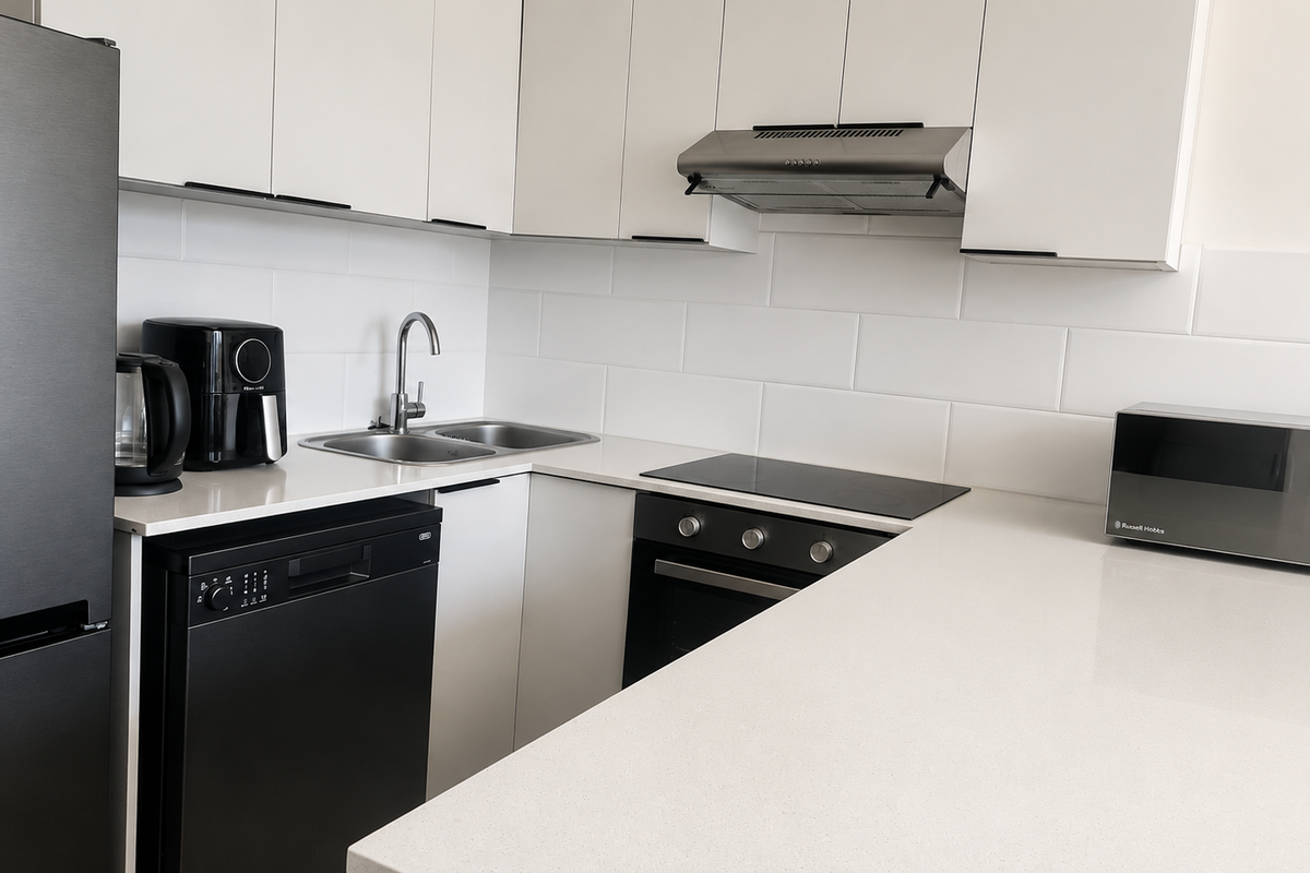 Modern kitchen featuring white cabinetry, stone countertops, subway tile backsplash, and integrated stainless steel appliances including an oven, hob, and extractor fan.