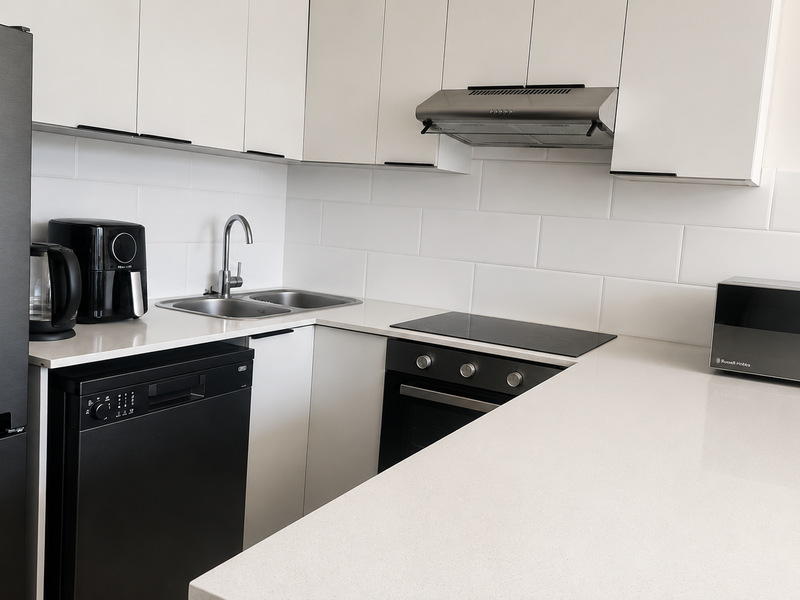 Modern kitchen featuring white cabinetry, stone countertops, subway tile backsplash, and integrated stainless steel appliances including an oven, hob, and extractor fan.