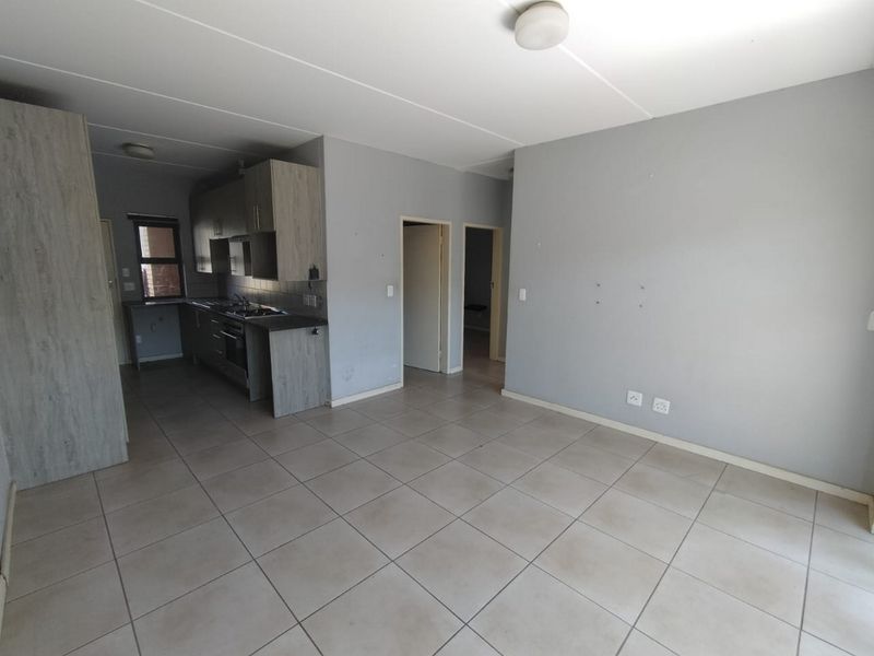 An open-plan living and kitchen area featuring tiled flooring, neutral grey walls, and functional built-in cabinetry with integrated cooking appliances.