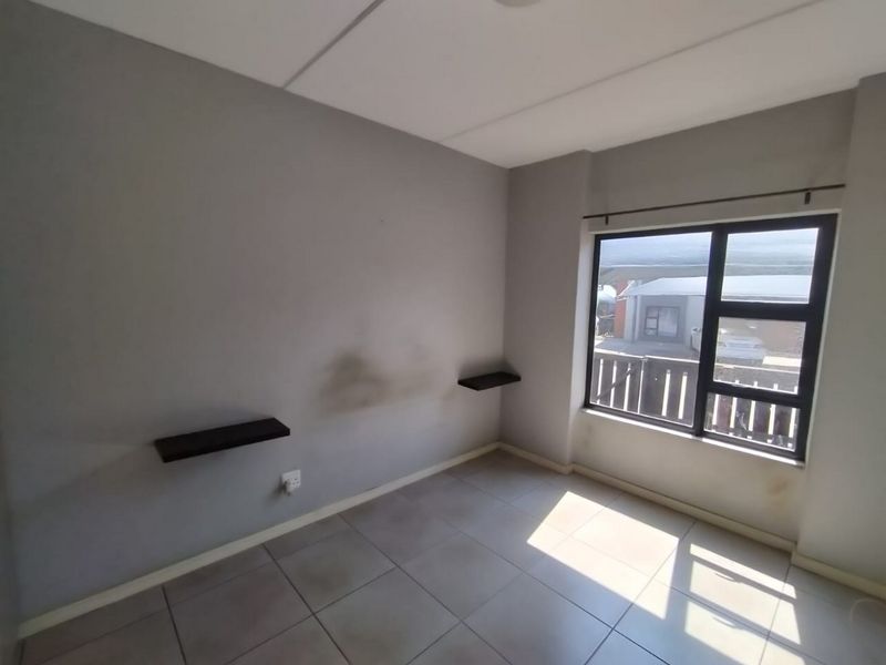An empty bedroom featuring tiled flooring, aluminium window frames, and wall-mounted floating shelves, requiring minor cosmetic attention to the walls.