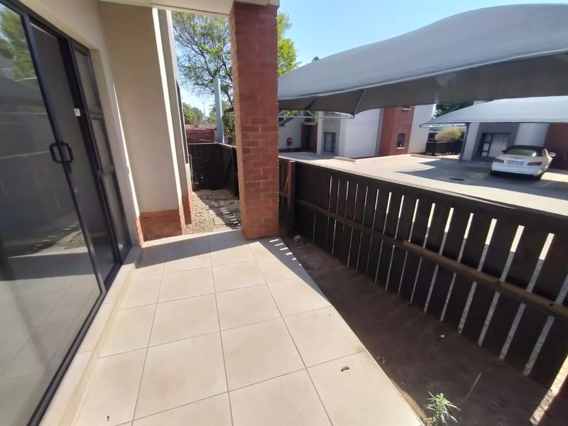 A covered patio area featuring tiled flooring and a brick support pillar, adjacent to a timber fence and outdoor parking area.