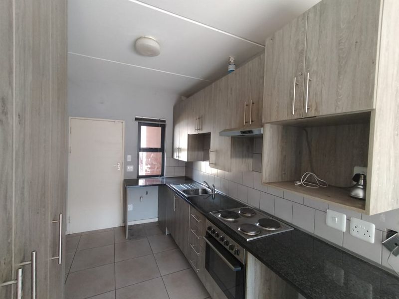 A functional kitchen featuring wood-look cabinetry, dark laminate countertops, a built-in electric oven and hob, and tiled flooring.