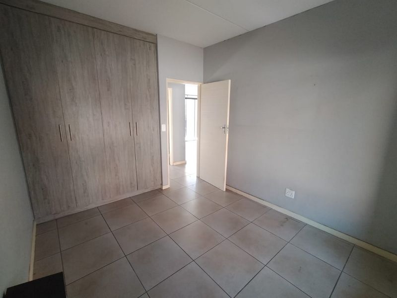 A clean, empty bedroom featuring neutral grey walls, tiled flooring, and ample built-in cupboard storage.