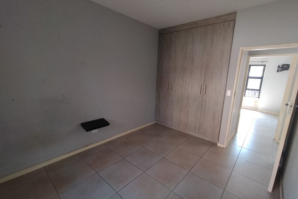 A vacant bedroom featuring neutral tiled flooring, built-in wooden cupboards, and a ceiling fan, offering a clean and functional space.