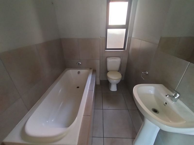 A functional bathroom featuring a bathtub, pedestal basin, and toilet with neutral wall and floor tiling.