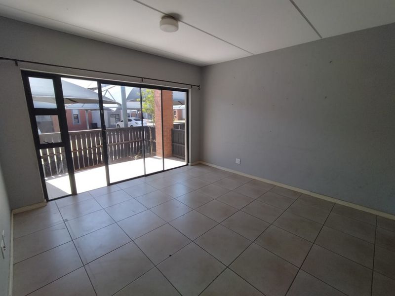 An empty living room featuring neutral tiled flooring and a large sliding glass door providing access to an outdoor patio area.