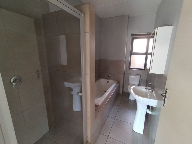 A functional bathroom featuring a separate shower enclosure, bathtub, pedestal washbasin, and toilet with neutral tiled finishes.