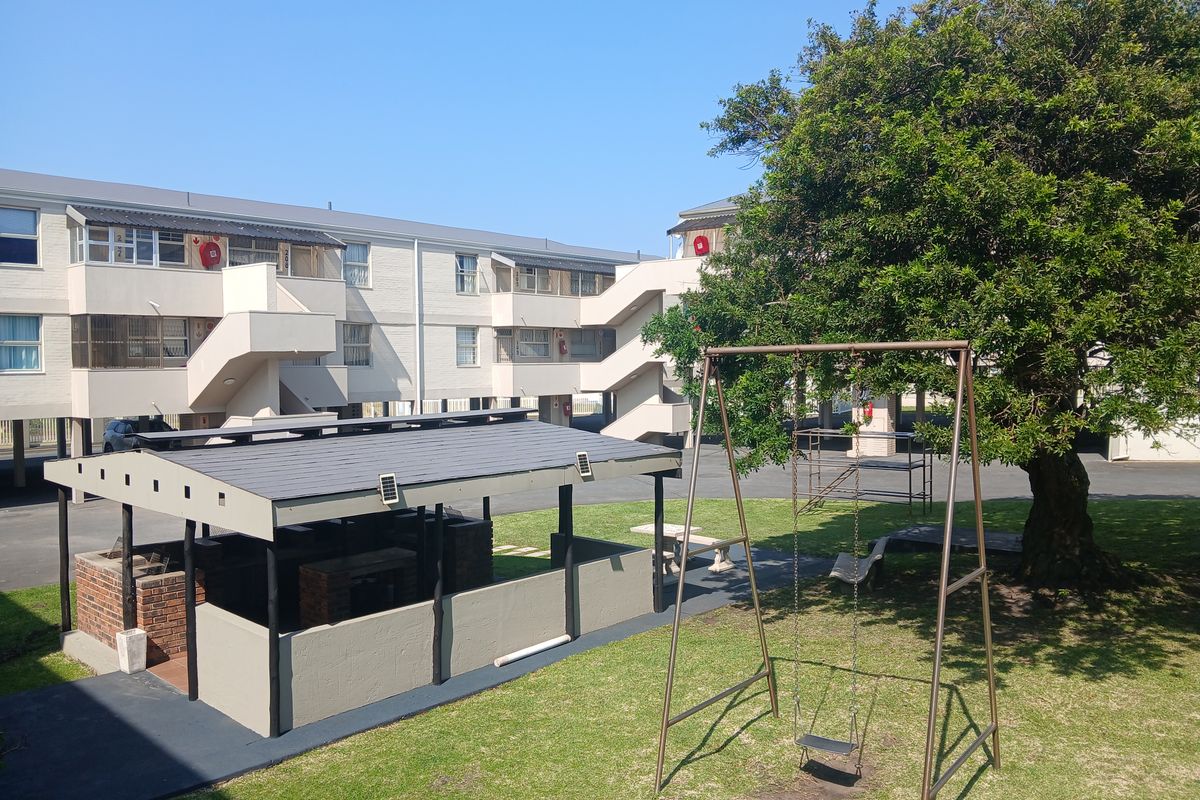 Communal outdoor area featuring a brick barbecue structure, swing set, and landscaped garden space within an apartment complex setting.