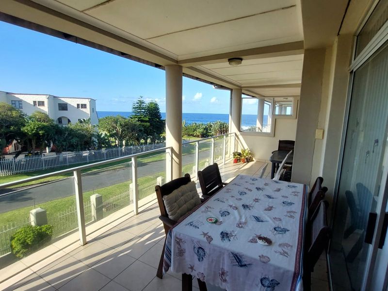 Spacious covered balcony featuring tiled flooring, a modern glass balustrade, and expansive views of the surrounding neighborhood and ocean.