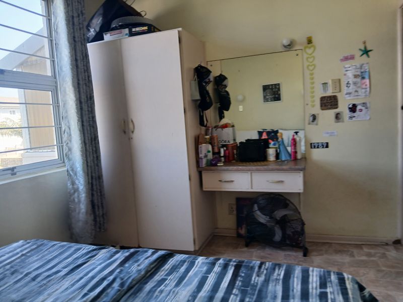 A bedroom featuring a built-in wardrobe and vanity unit with a large mirror, complemented by an aluminium window with security bars.