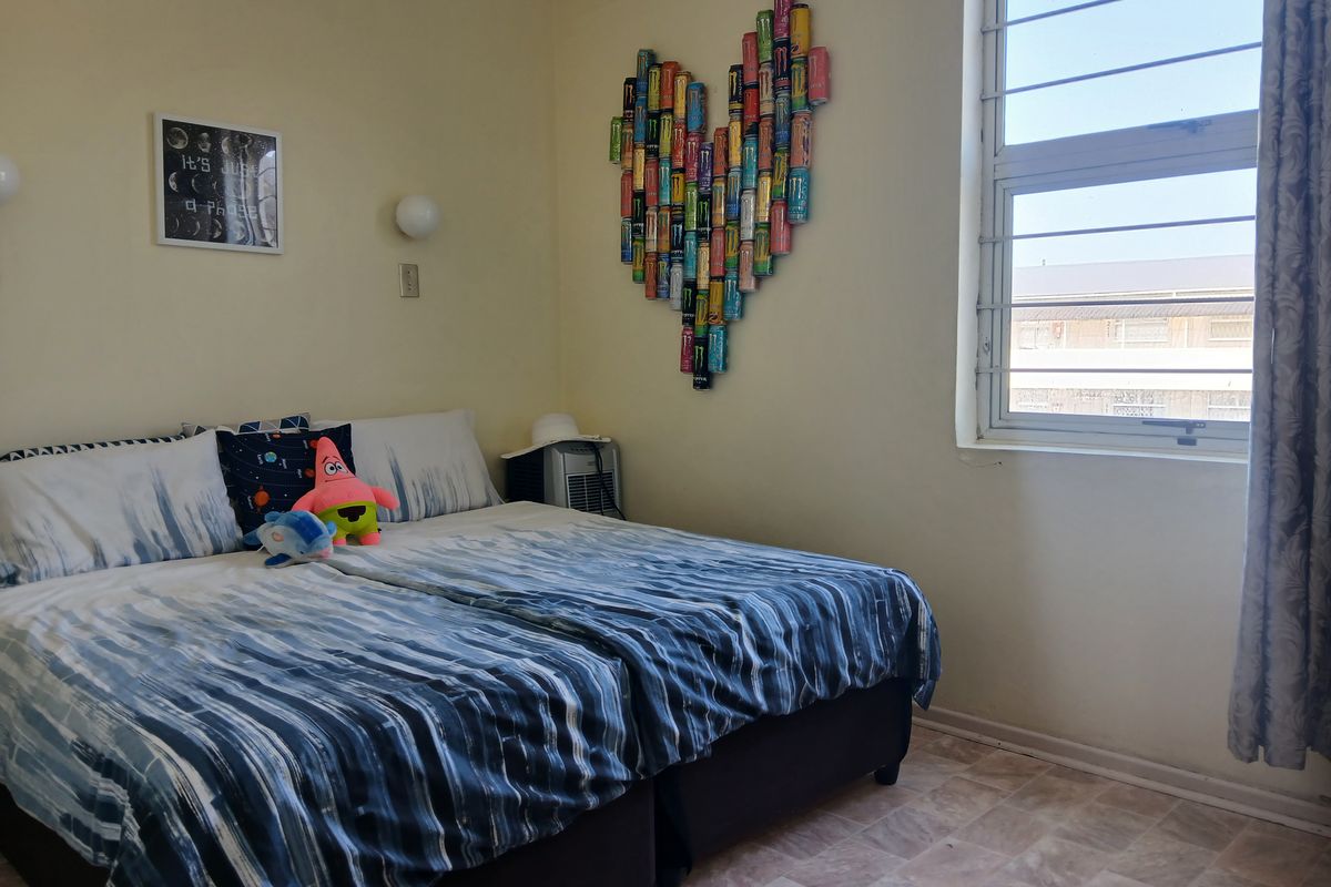 A bedroom featuring tiled flooring, wall-mounted lighting, and a window fitted with security bars.