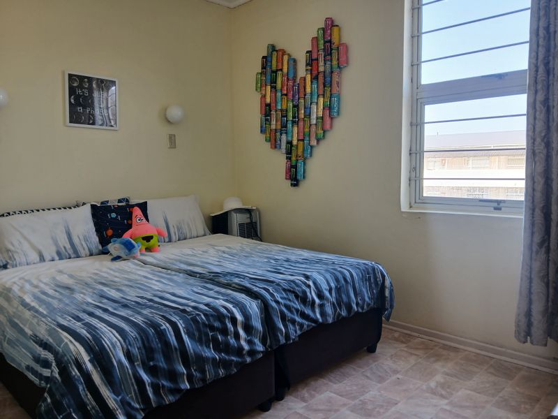 A bedroom featuring tiled flooring, wall-mounted lighting, and a window fitted with security bars.