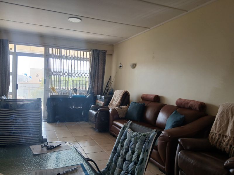 A living room area featuring tiled flooring and a sliding glass door with a security gate, providing access to an outdoor space.