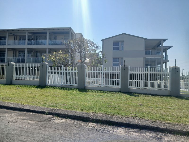 Front view of a modern apartment complex featuring white perimeter fencing, electric security, and private balconies with glass balustrades.