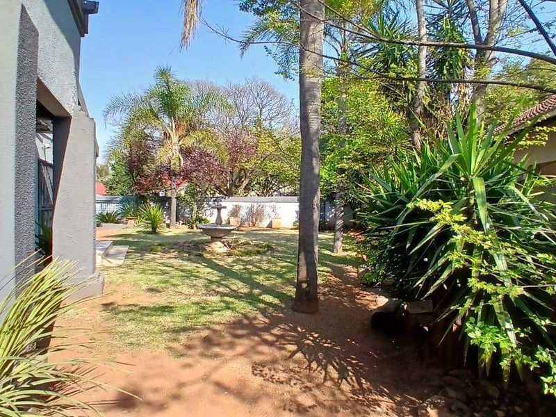 A spacious rear garden featuring a central stone fountain, mature trees, and established landscaping enclosed by a boundary wall.