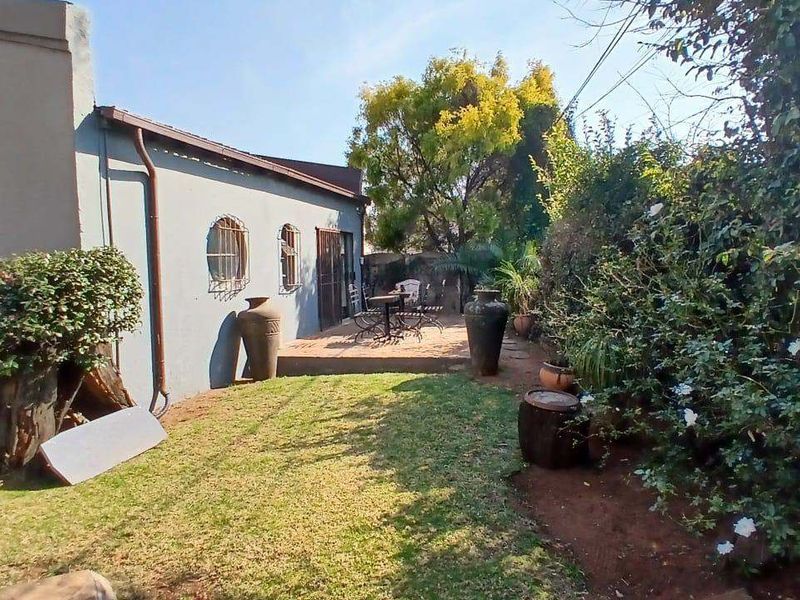 Rear view of the property featuring a small tiled patio area, established garden, and exterior wall access with security bars on windows.