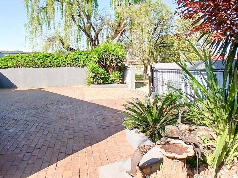 A paved front driveway area featuring a boundary wall, metal gate, and established garden landscaping.