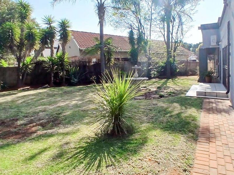 A rear garden area featuring a brick paved walkway, established trees, and a central stone fountain feature.