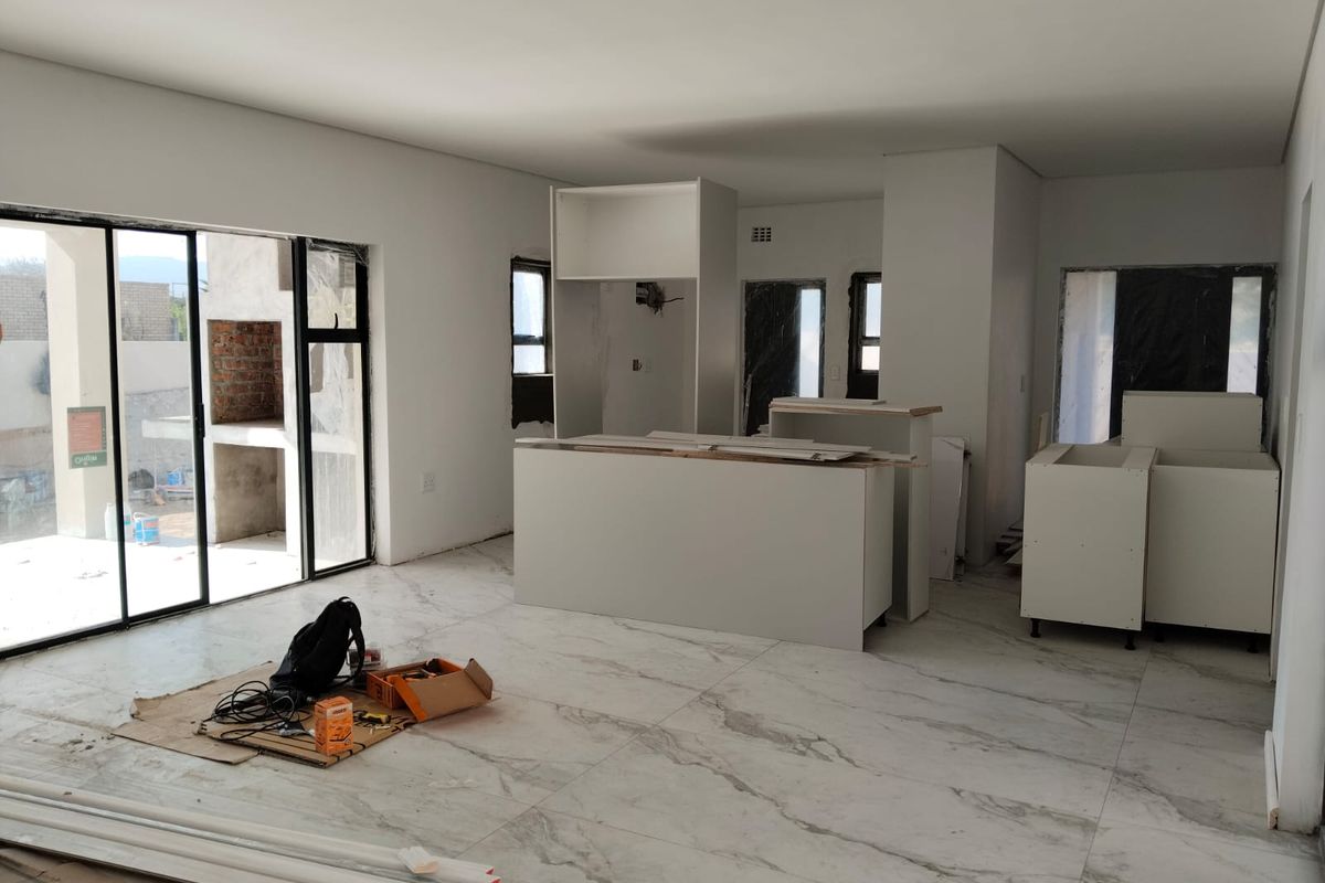 Open-plan living and kitchen area currently under construction, featuring large format marble-look floor tiles and sliding door access to an outdoor patio.