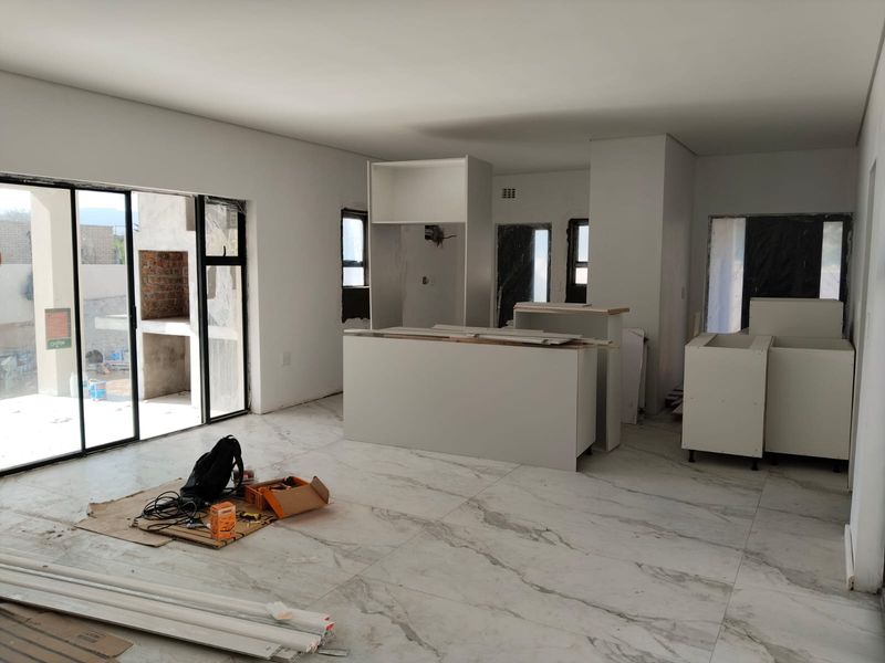 Open-plan living and kitchen area currently under construction, featuring large format marble-look floor tiles and sliding door access to an outdoor patio.