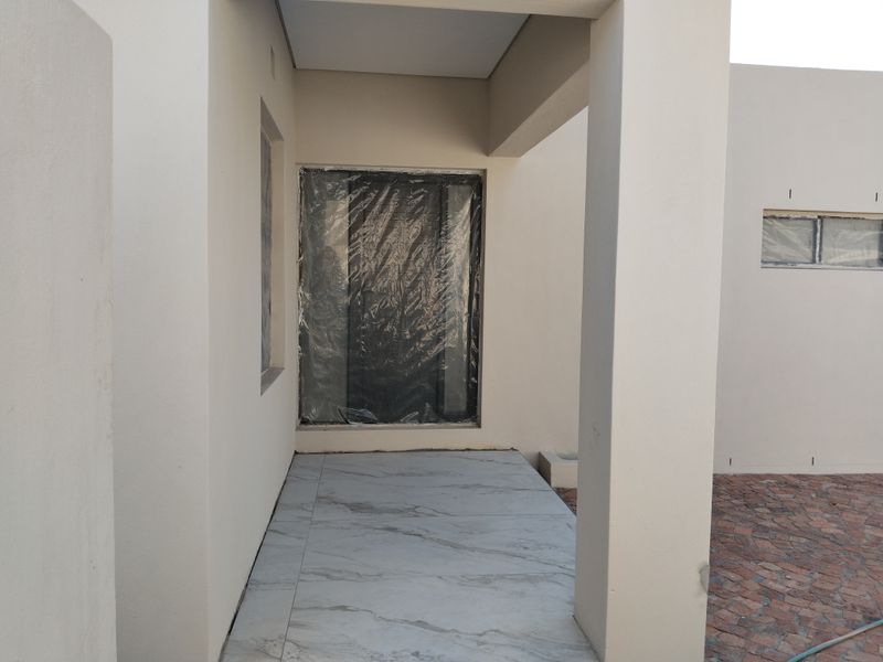 A covered entrance area featuring modern tiled flooring and structural pillars, currently undergoing final finishing touches with window protection still in place.