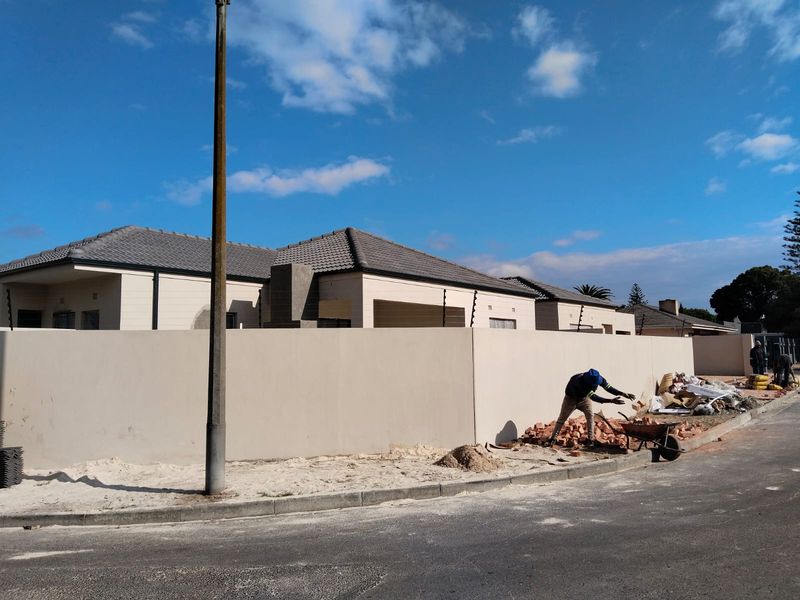 Front view of a townhouse complex featuring a perimeter wall with electric fencing and ongoing exterior construction work.
