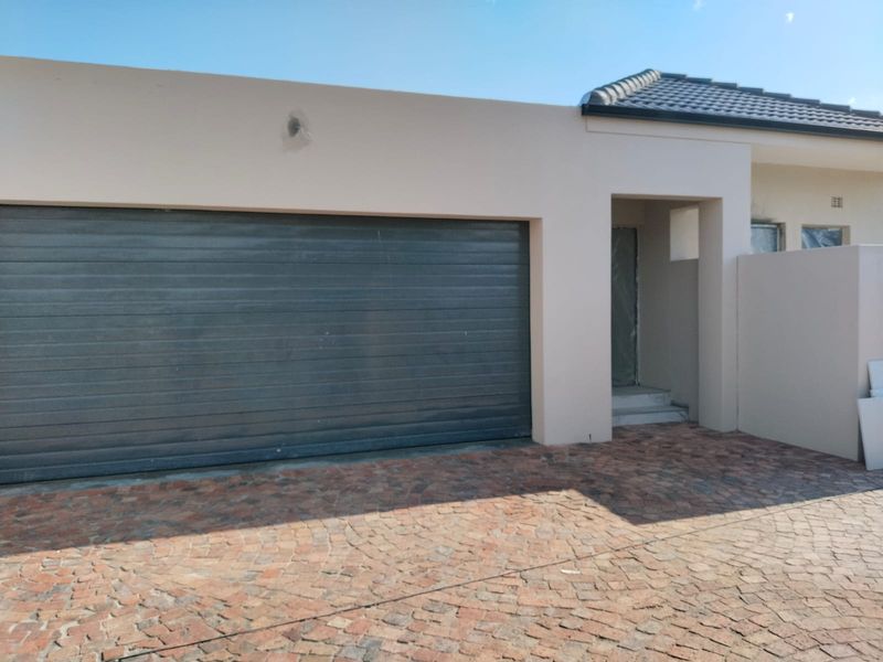 Front exterior view of a townhouse featuring a double garage, paved driveway, and modern plastered facade.