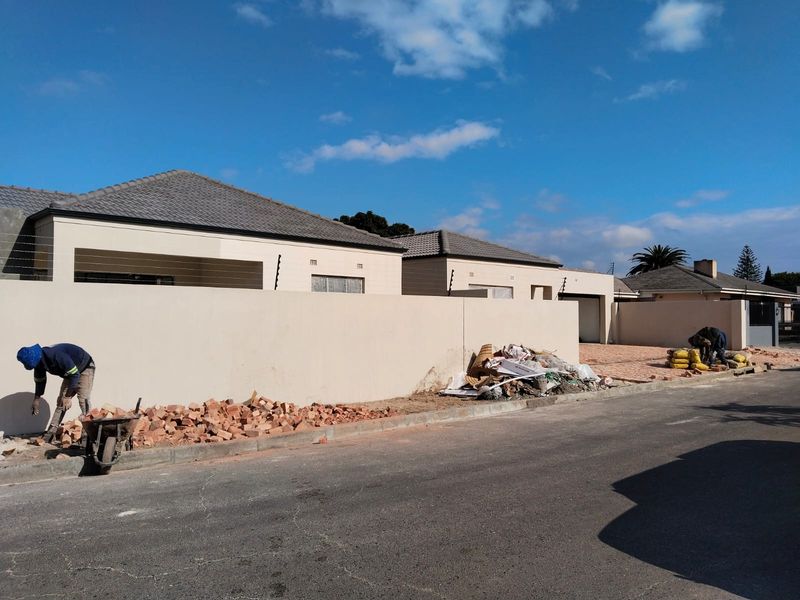 Front exterior view of a townhouse complex showing perimeter walls, electric fencing, and ongoing paving work on the driveway.