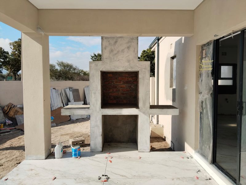 A covered patio area currently under construction, featuring a central built-in braai and partially installed floor tiles.