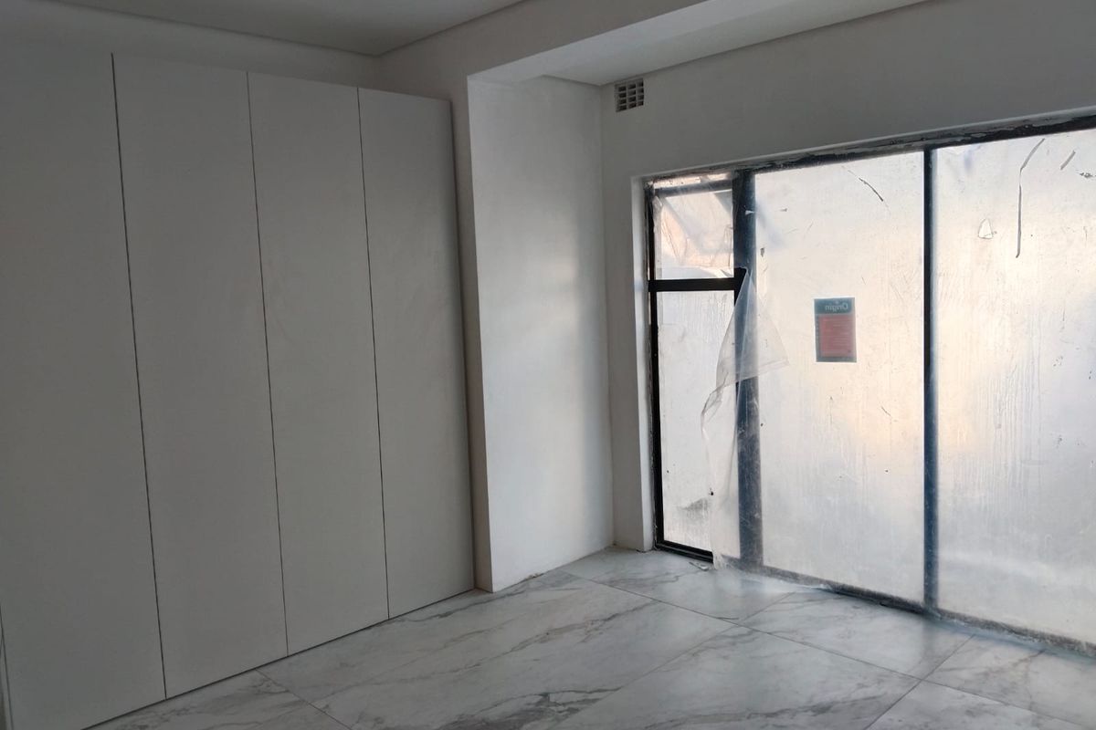 A modern, empty bedroom featuring sleek built-in cupboards, marble-look tiled flooring, and a large sliding glass door leading to an outdoor area.