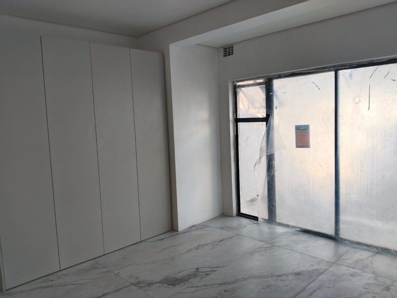 A modern, empty bedroom featuring sleek built-in cupboards, marble-look tiled flooring, and a large sliding glass door leading to an outdoor area.